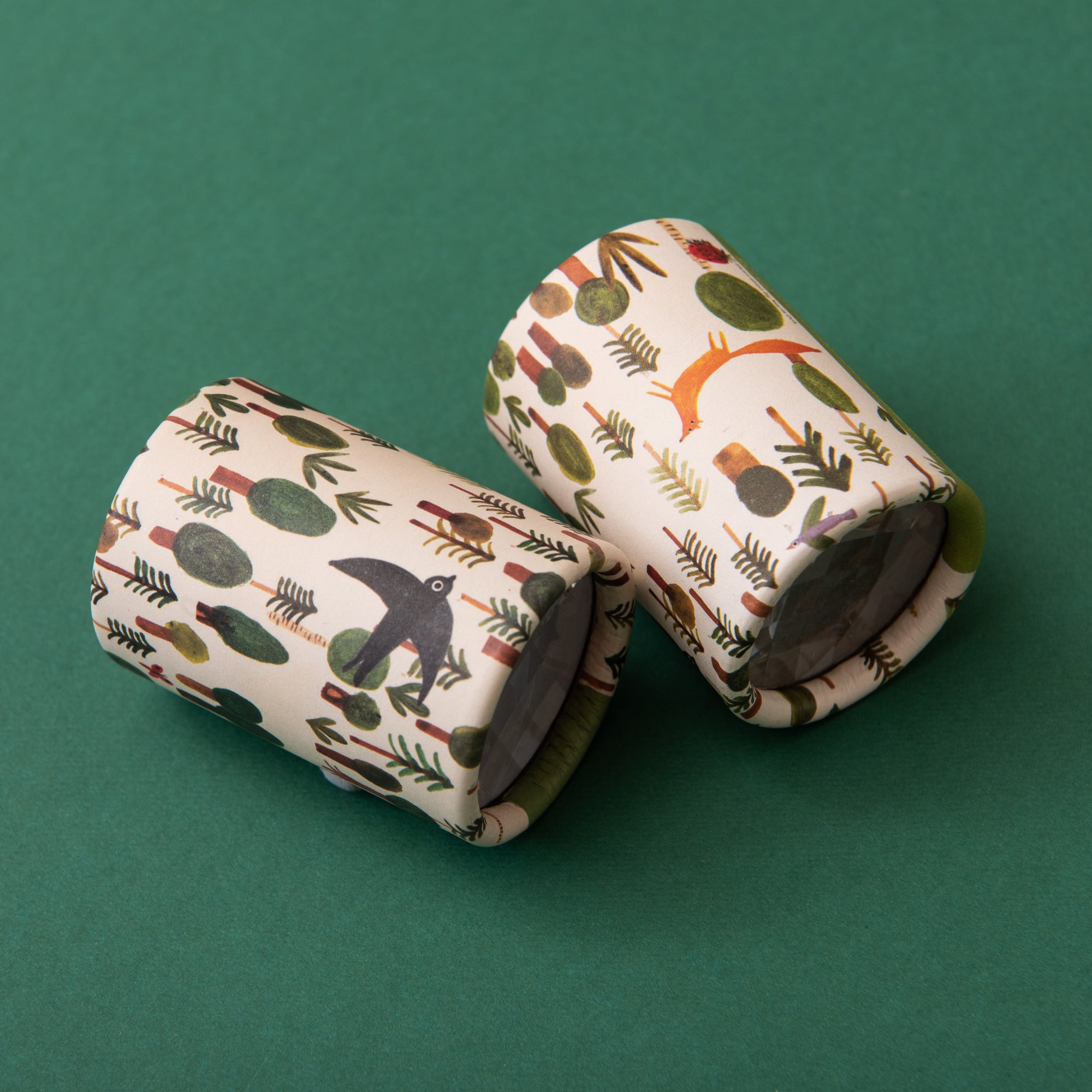 Two cylindrical Kaleidoscopes with nature-themed patterns on a green background