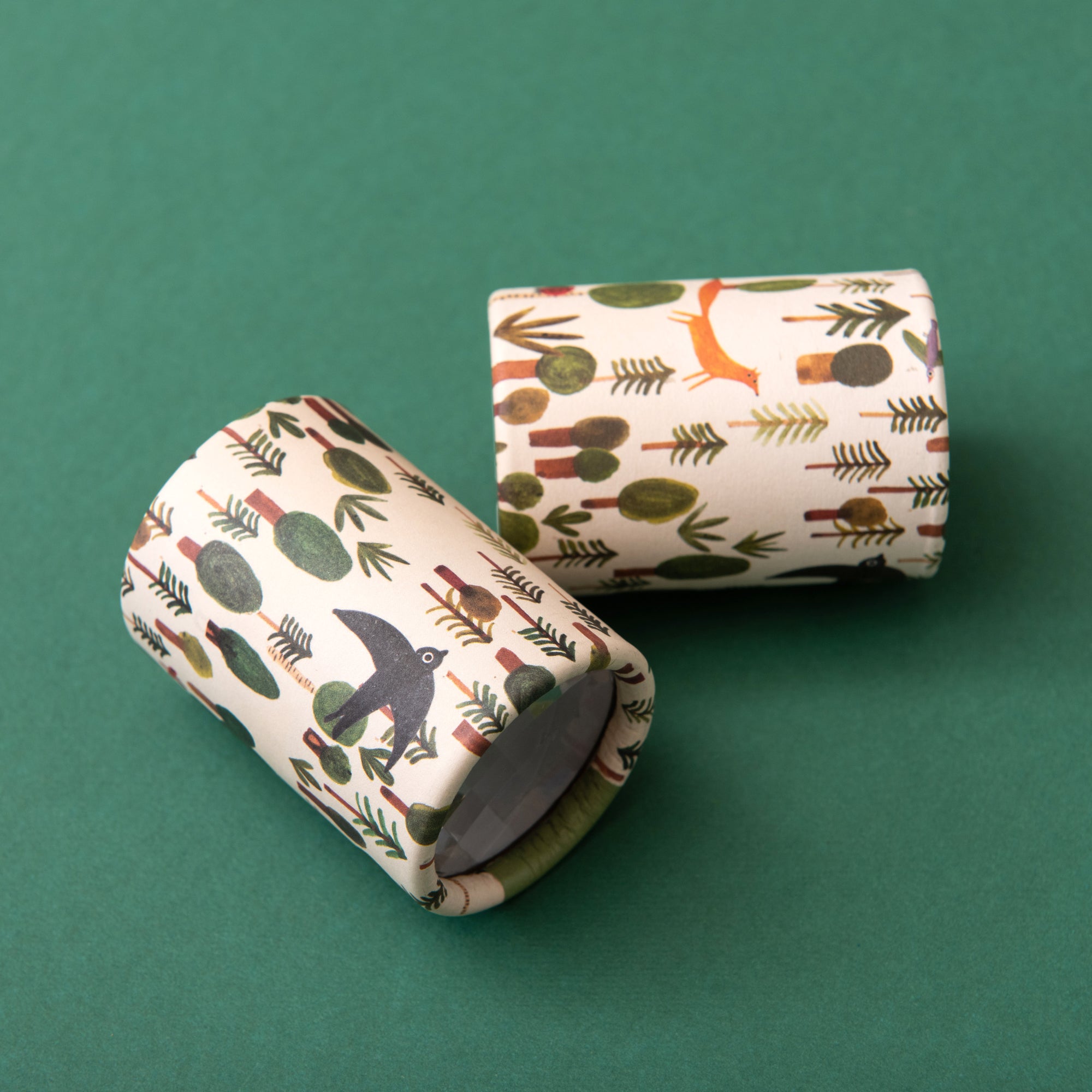Two cylindrical Kaleidoscopes with nature-themed designs on a green background