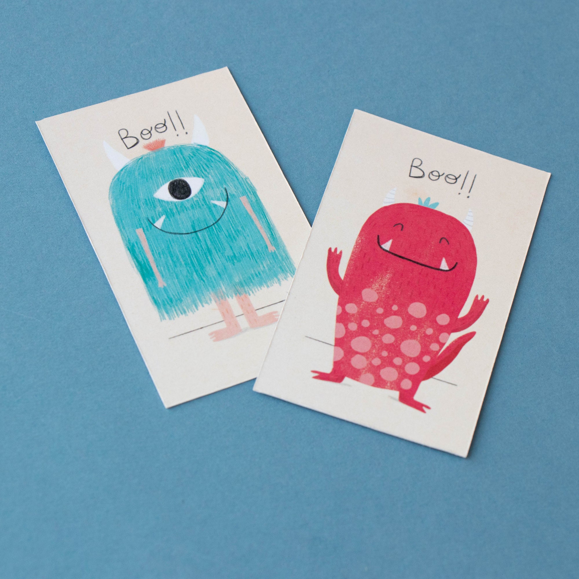 Two greeting cards with colorful monster designs on a blue background
