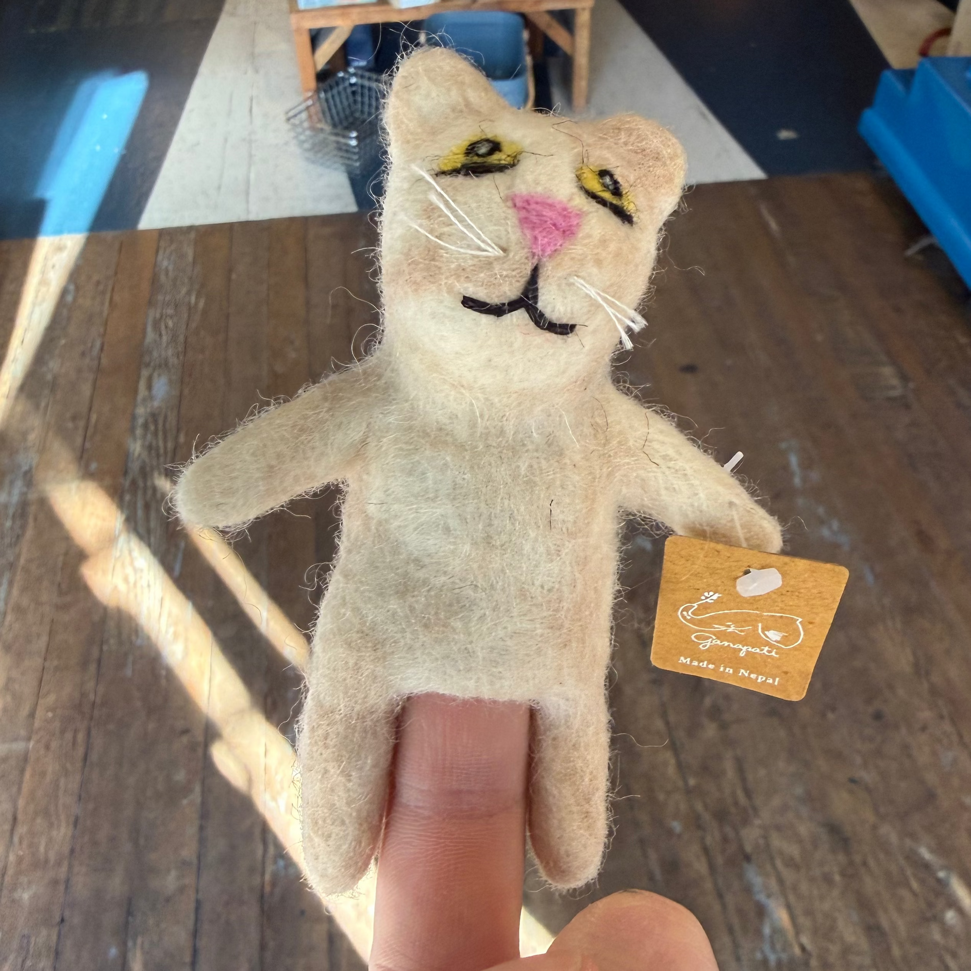 Small cat-shaped plush toy held by a finger with a store interior in the background