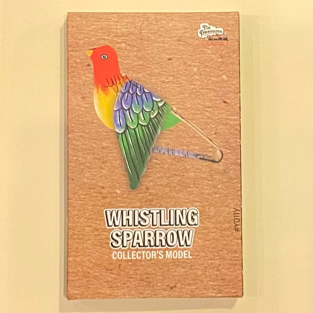 Colorful bird figurine on a wooden background with 'Whistling Sparrow' text.