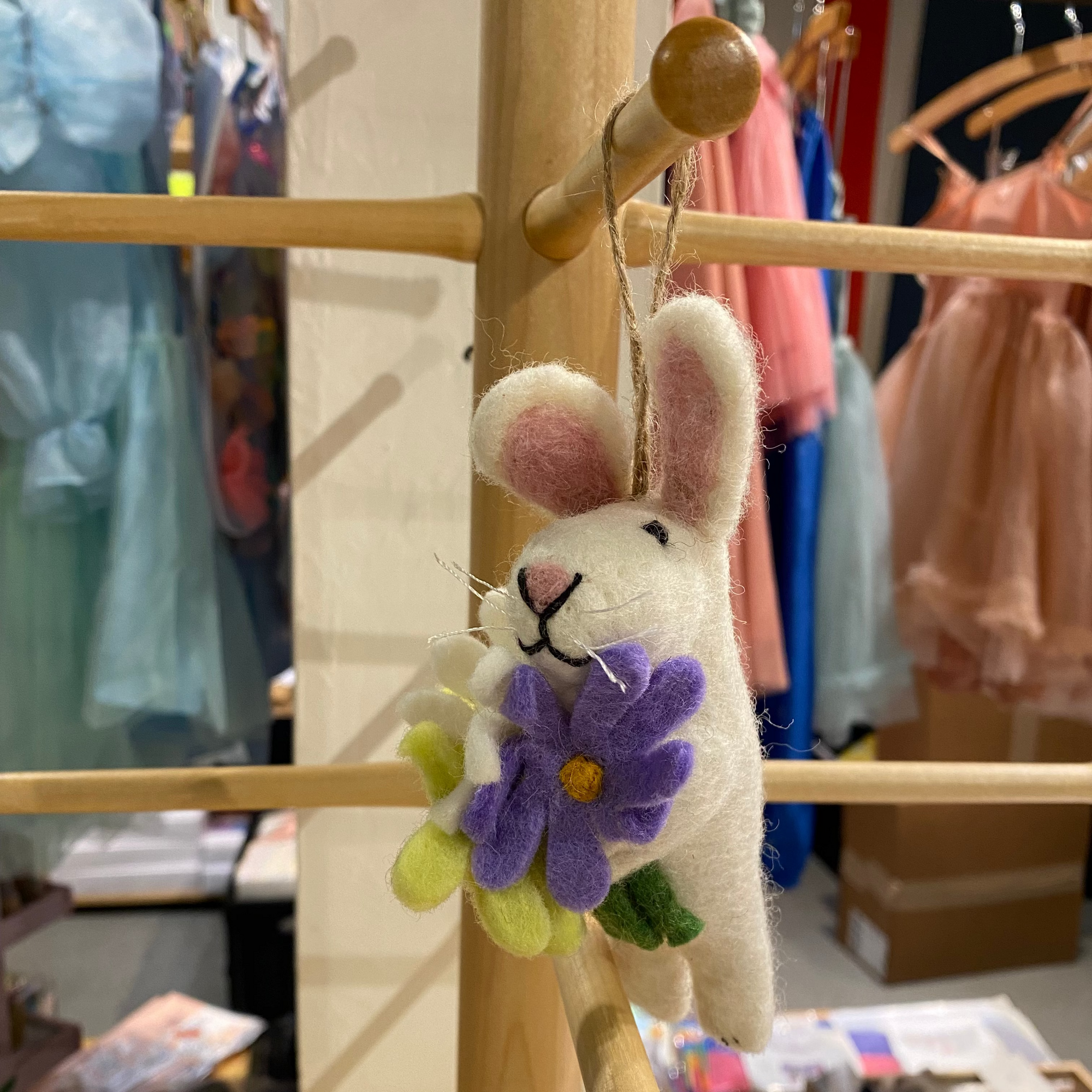 Plush bunny toy with a flower hanging on a wooden rack in a store setting.