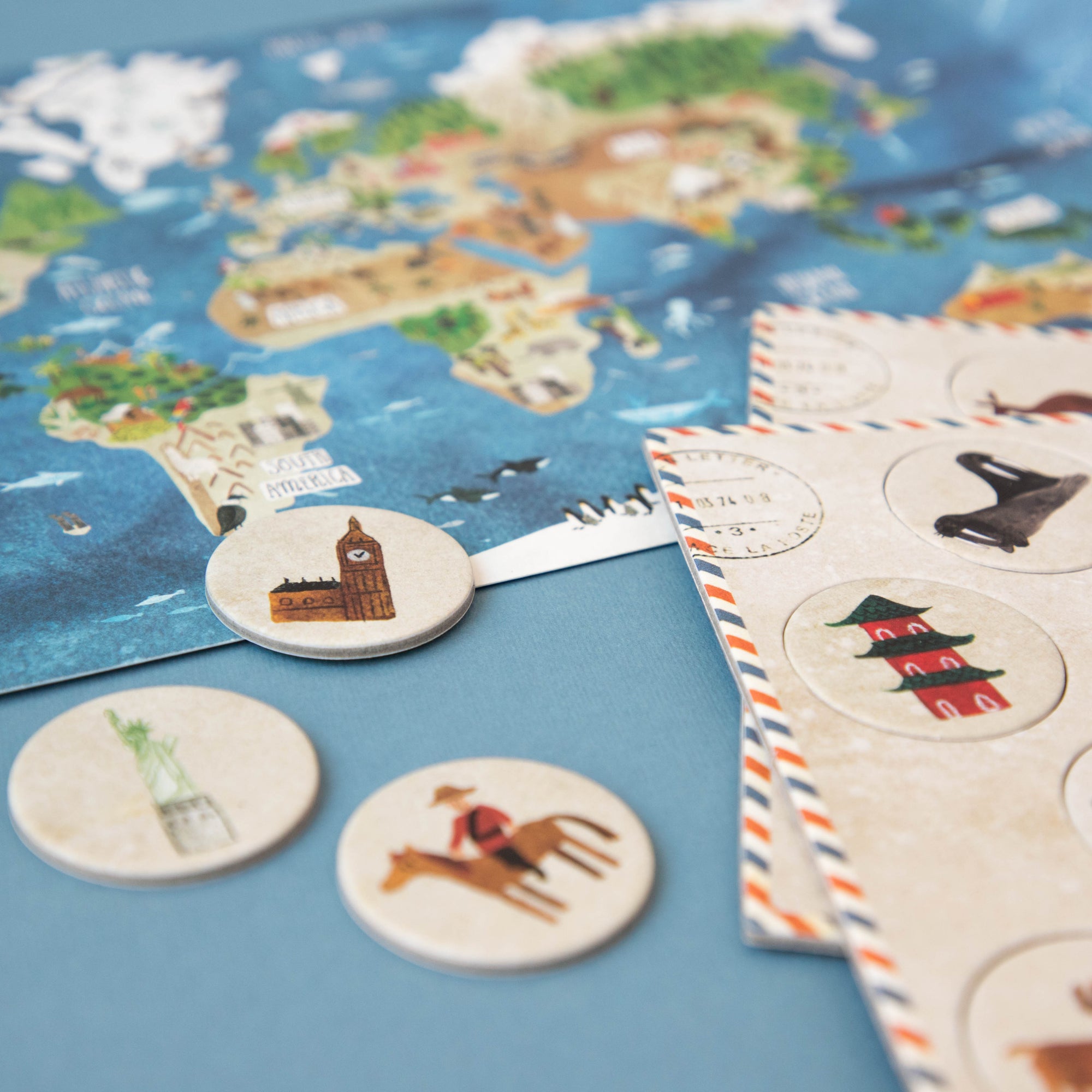 World map with travel-themed coasters and a stack of cards on a blue surface