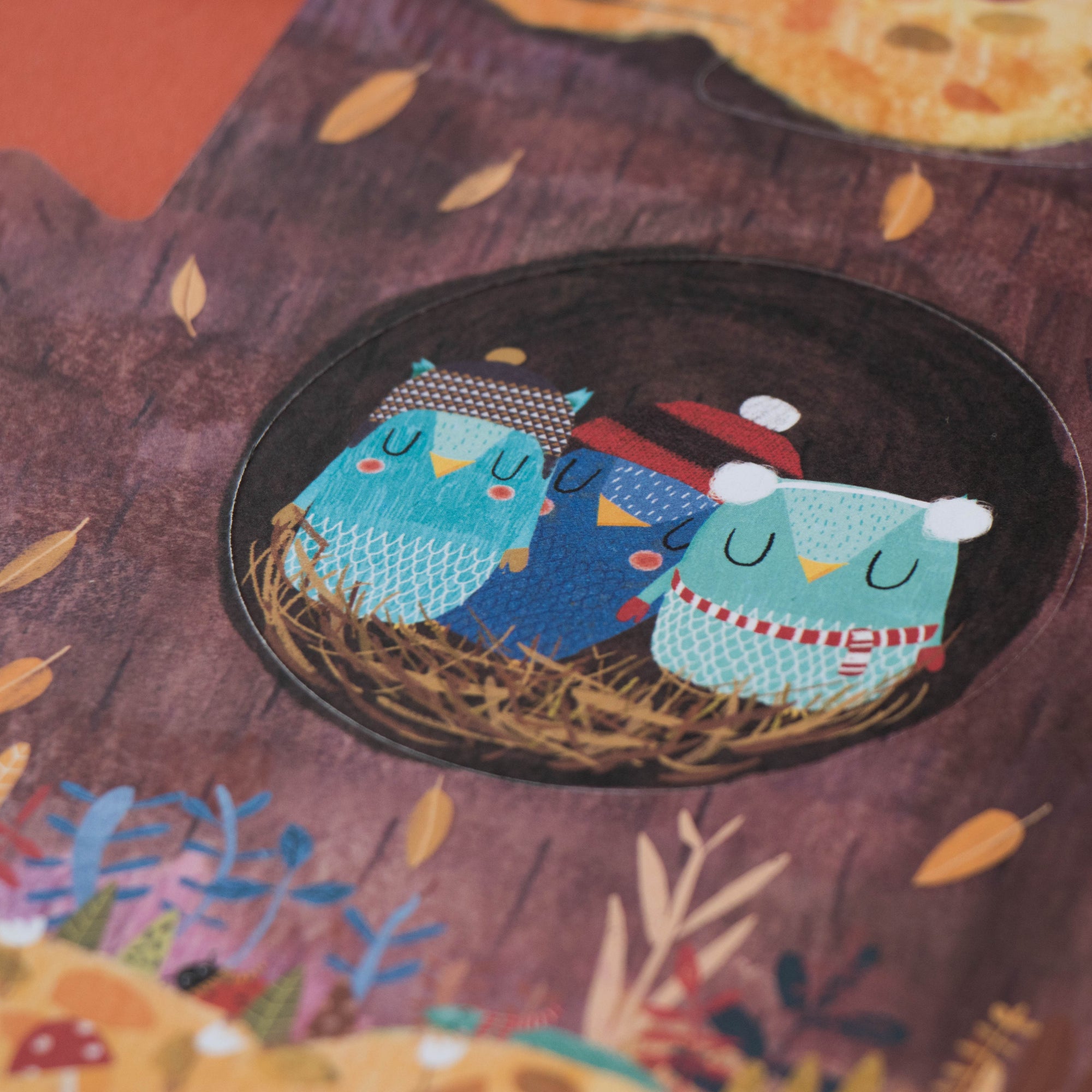 Illustration of three blue birds in a nest with autumn leaves and flowers on a brown background