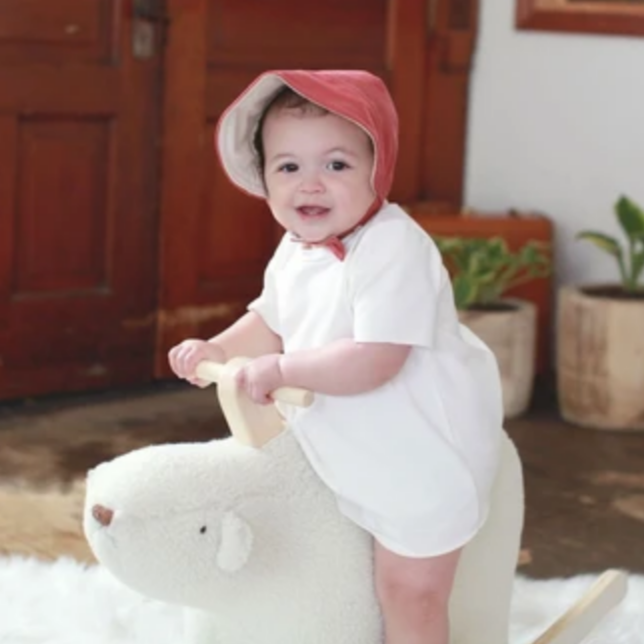 smiling baby riding polar bear toy wearing red sun bonnet