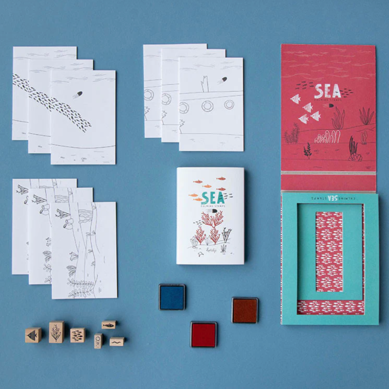 A set of wooden stamps with sea-themed designs, including fish and coral, displayed alongside fold-out sheets and ink pads in red, blue, and green colors.