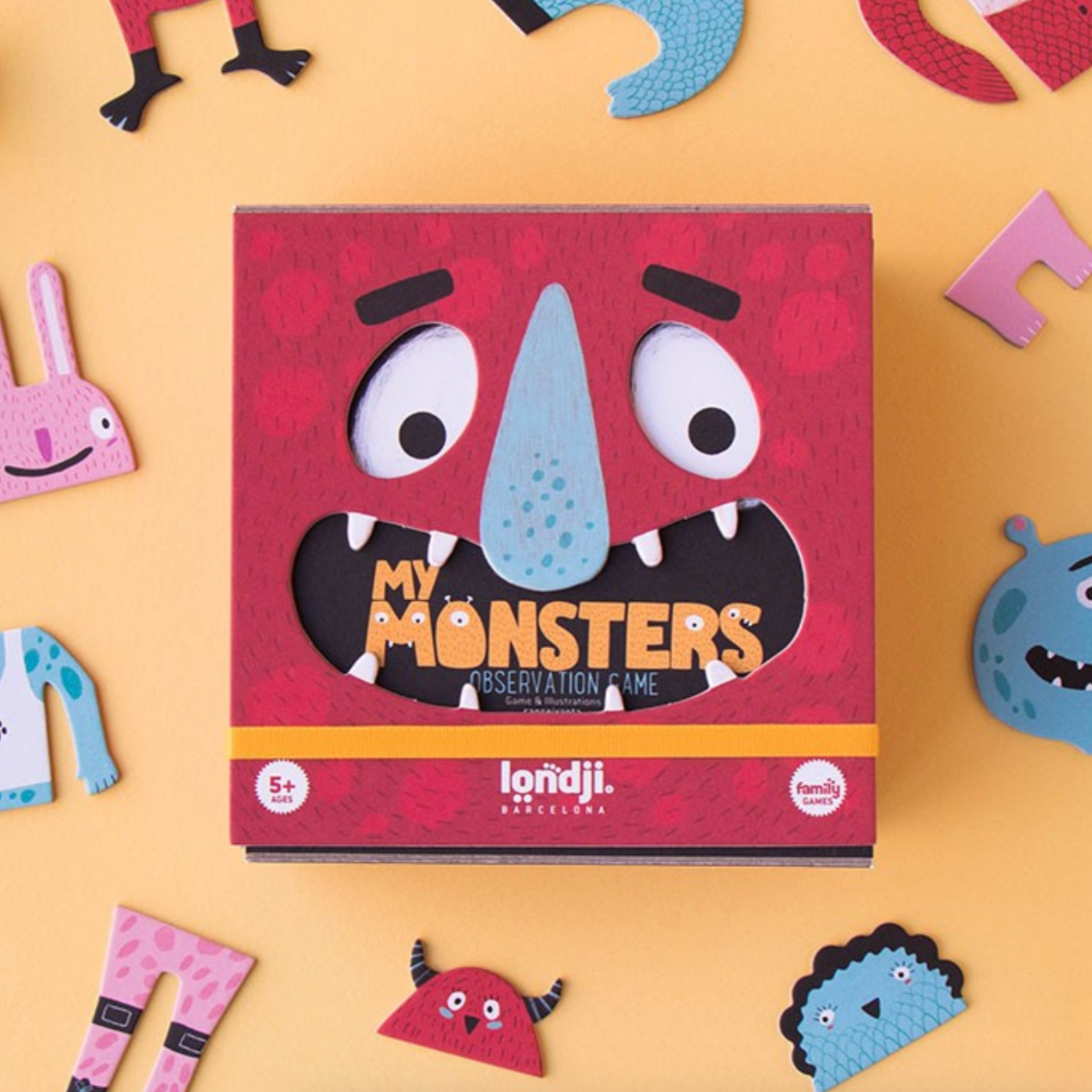The image shows the board game 'My Monsters' by Londji, which includes various colored cardboard monster parts scattered around the box that has a cartoonish monster face design.