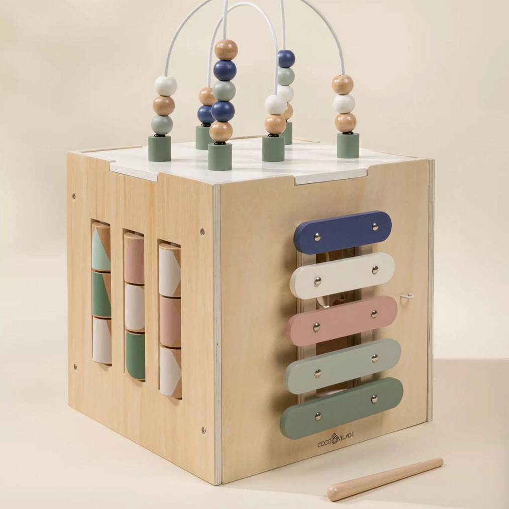 A wooden activity cube with various playful mechanical elements on each side, including beads on a track, buttons, and a marbles run.