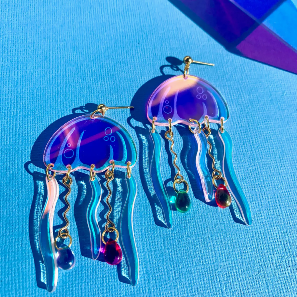 A pair of colorful jellyfish-shaped earrings with gold-plated ball posts, displayed against a blue background.