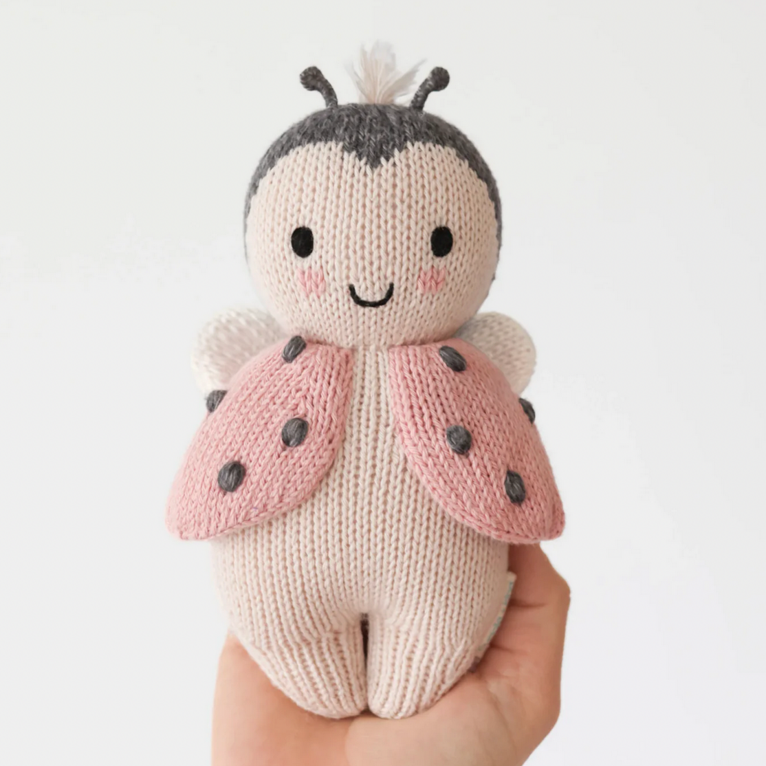Knitted ladybug toy held by a hand on a white background