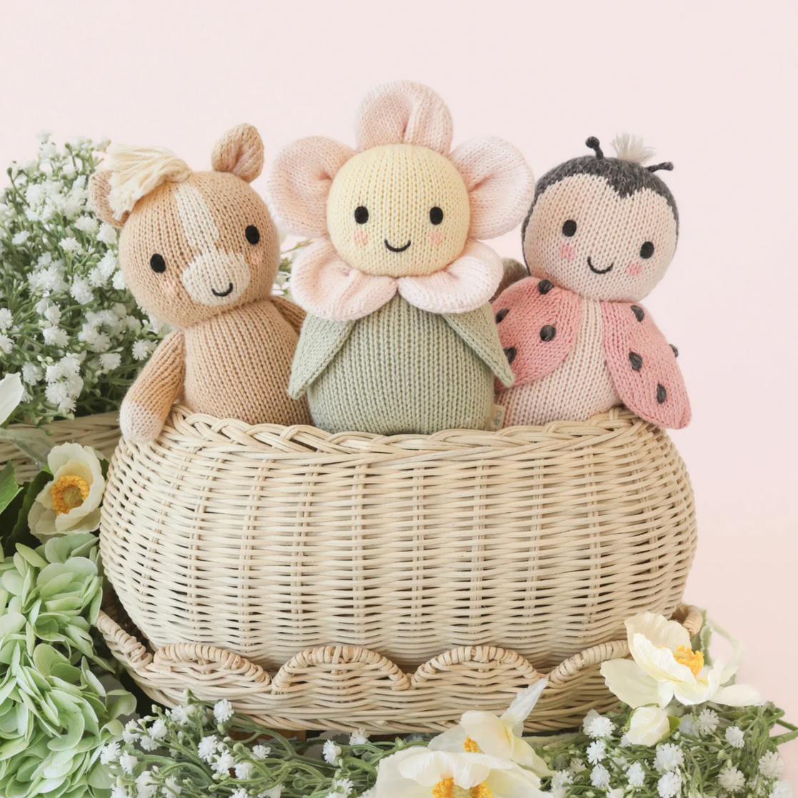 Three knitted toys in a basket with a soft pink background