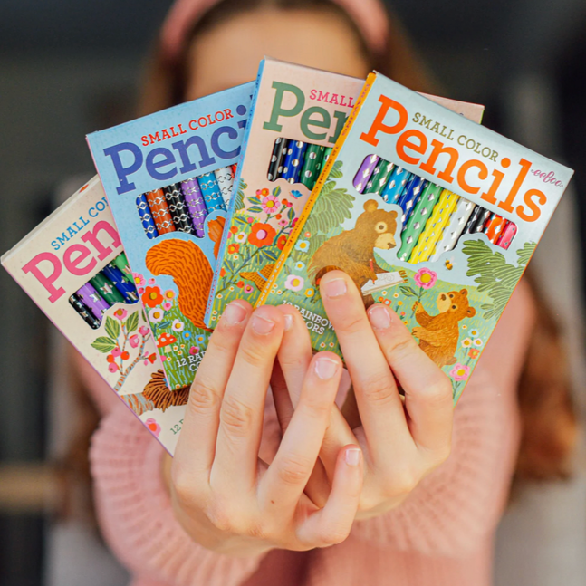 Hands holding small color pencil books with animal illustrations on a blurred background