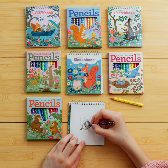 Colorful children's sketchbooks and pencils on a wooden table with a hand drawing.
