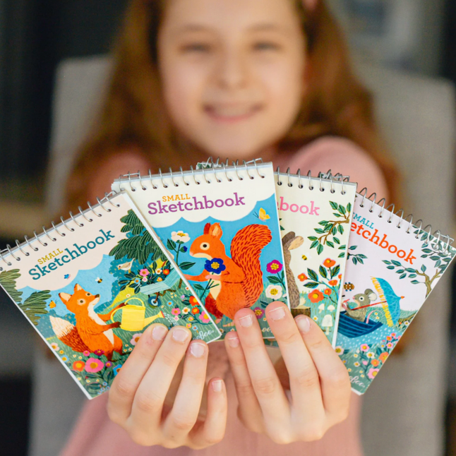 Child holding a set of colorful sketchbooks with animal illustrations.