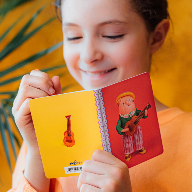 Child holding a colorful book with illustration of a pig playing a guitar and a guitar.