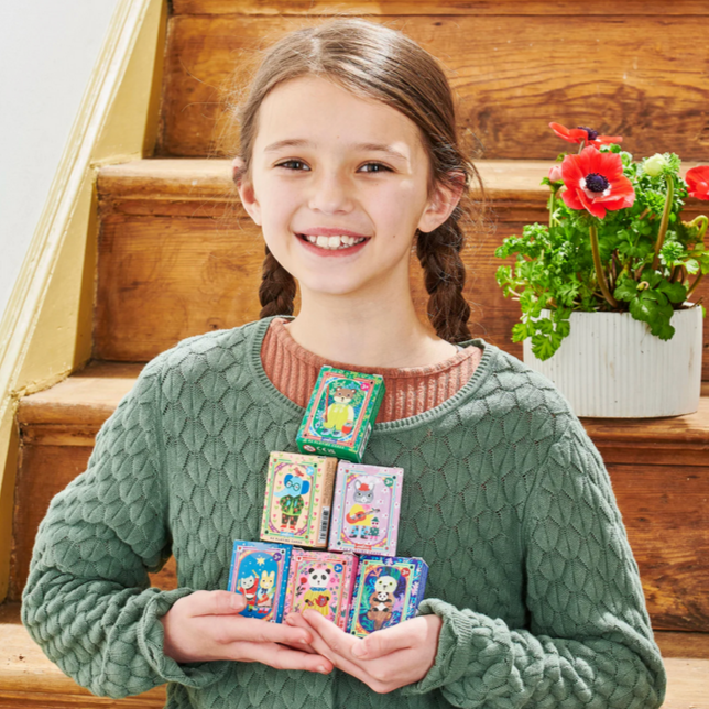 Young girl holding colorful cards on a wooden staircase with a plant in the background