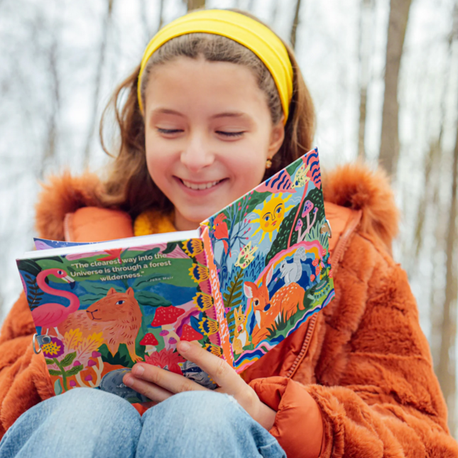 Child reading a colorful journal with a forest design, sitting outdoors.