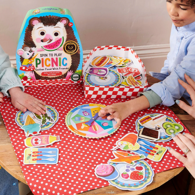 Children playing with a toy picnic set on a red polka dot tablecloth.