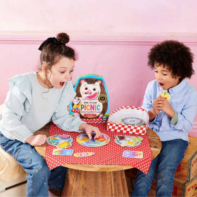 Two children playing with a toy picnic set on a small table.
