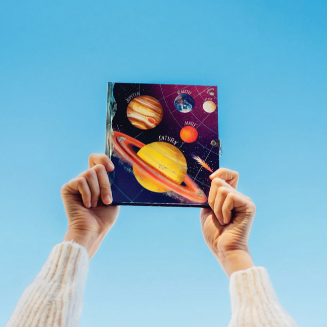Person holding a journal with space-themed cover against a blue sky
