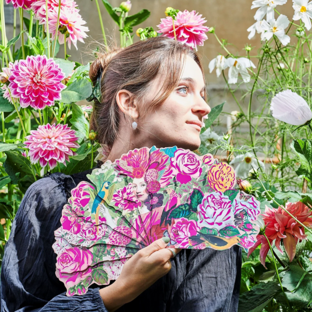 Woman holding a floral fan in a garden setting .