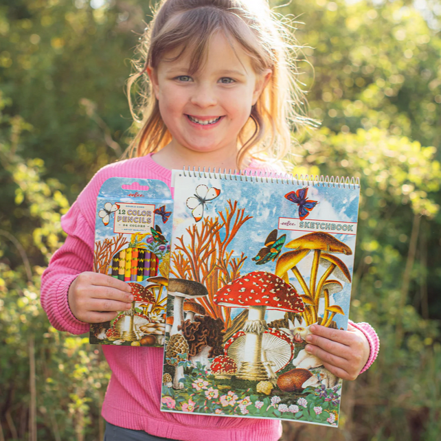 Child holding a sketchbook with matching pencils and nature-themed designs outdoors