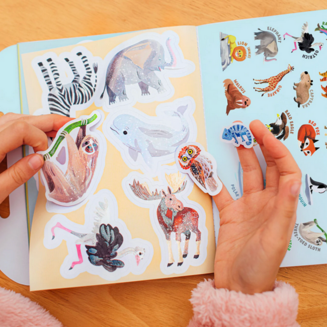 Sticker book with animal stickers and hands holding some of them on a wooden surface.