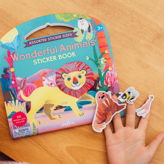 Sticker book with animal illustrations on a wooden surface, with a hand holding stickers.