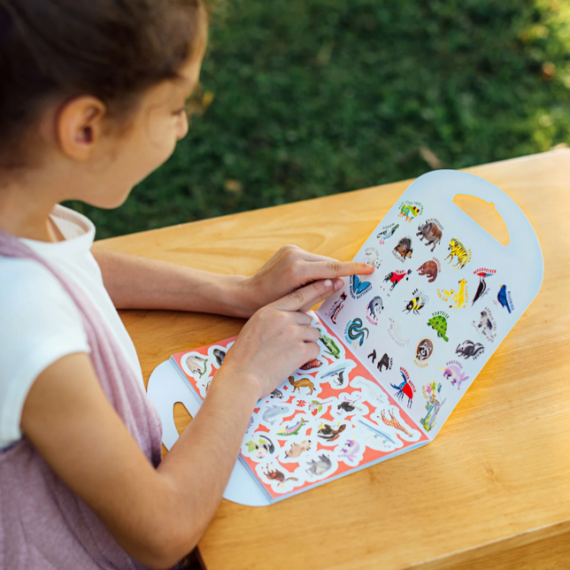 Child looking at a sheet of stickers on a wooden table outdoors