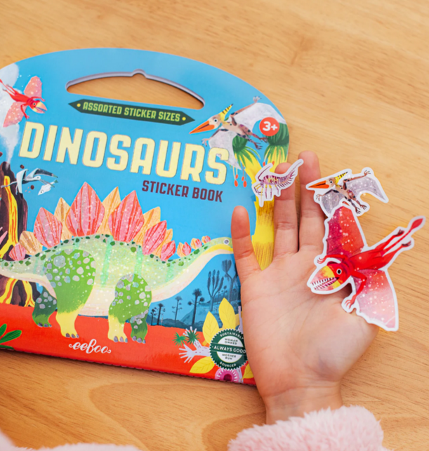 Dinosaurs sticker book with colorful cover and a hand holding a sticker on a wooden surface
