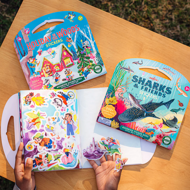 Sticker books with 'Sharks & Friends' and 'Holiday & Woods' on a wooden table.