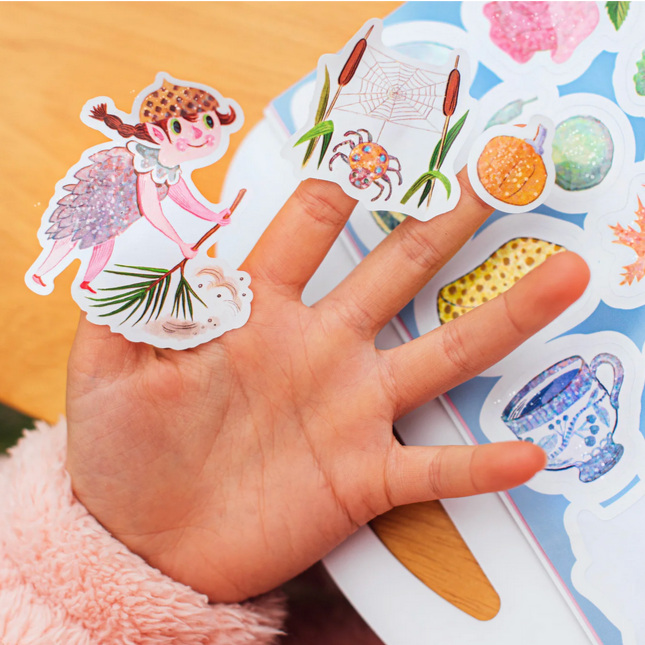Hand holding a sheet of colorful stickers with various designs on a wooden background