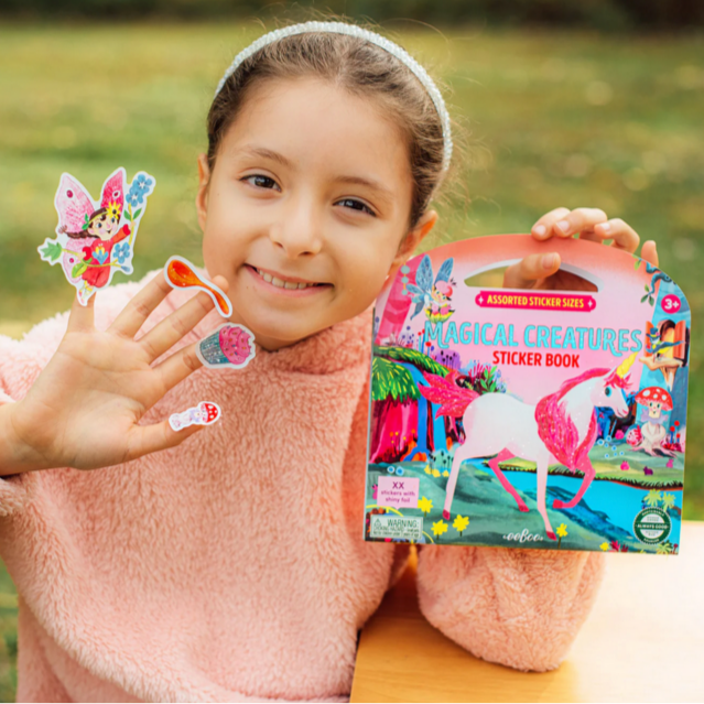 Child holding a 'Magical Creatures' sticker book and stickers outdoors