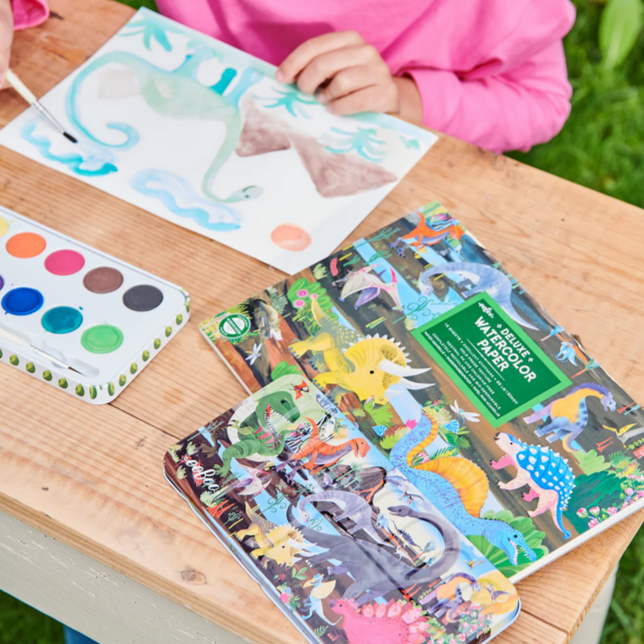 Children's paints and painting supplies on a table outdoors.