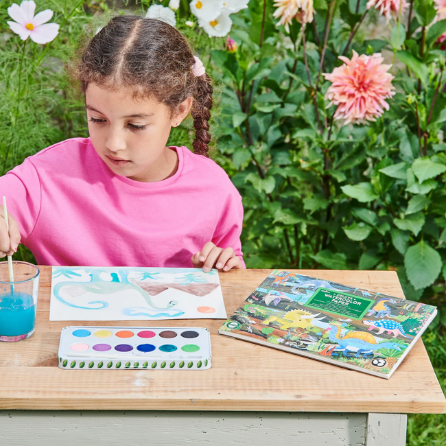 Child painting with a book and art supplies outdoors