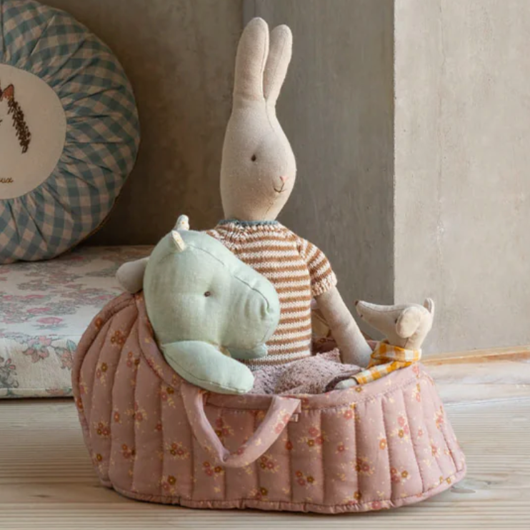 Stuffed rabbit and turtle toys in a pink basket on a wooden surface with a checkered pillow in the background.
