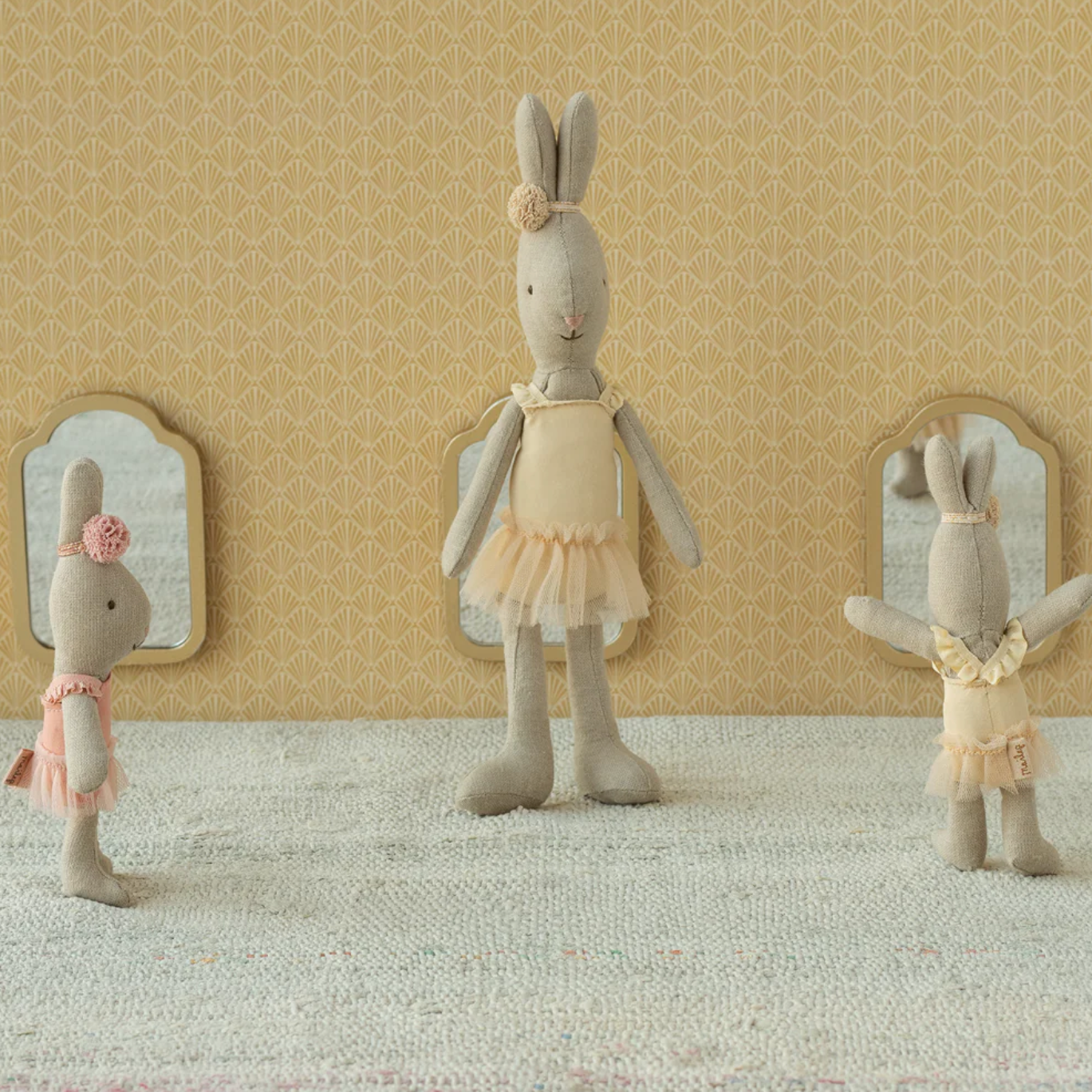 Three stuffed rabbit toys in a decorative setting with mirrors and a patterned wall.