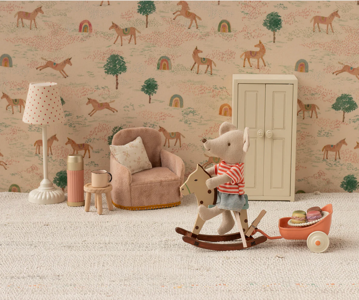 Children's room with wallpaper featuring animals, a teddy bear on a rocking horse, and a lamp.