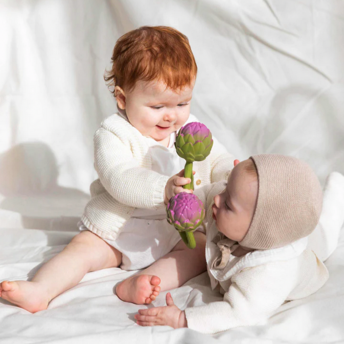 Two babies playing with a flower teether on a white fabric background