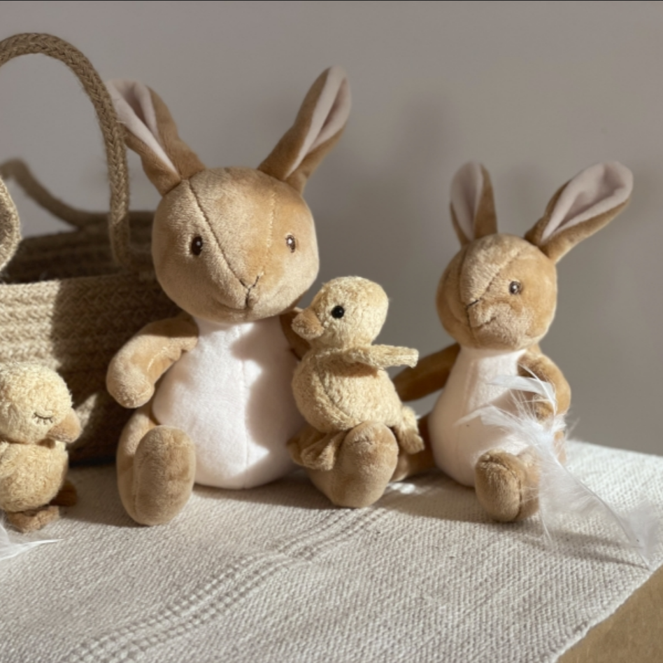 Set of plush bunnies and a teddy bear with a woven basket on a textured surface.