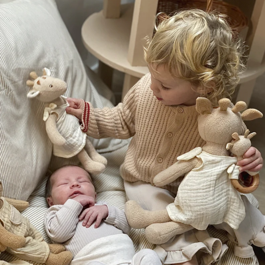 Two children playing with stuffed giraffes on a bed
