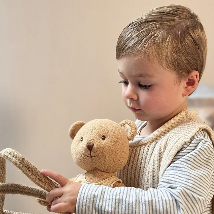 Child holding a teddy bear and a woven basket against a neutral background