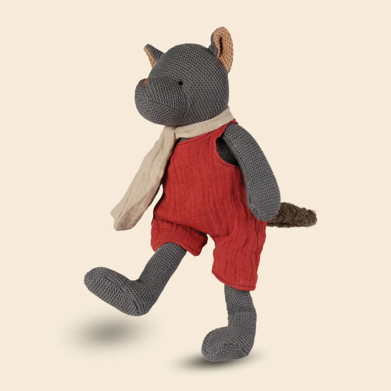 Knitted toy fox in red overalls on a beige background