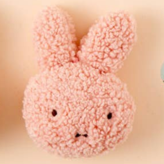 Pink bunny-shaped plush toy on a beige background with small bunny stickers.