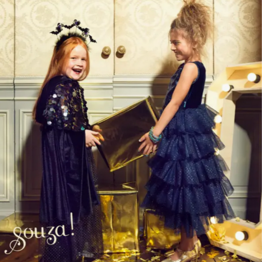 Two children in formal navy dresses opening a gold box in an elegant room.