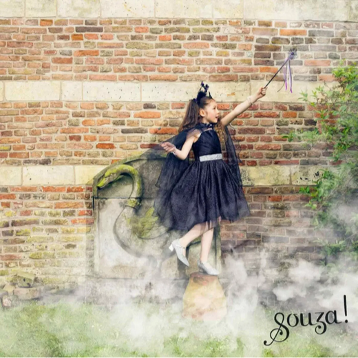 Young girl in a dark dress standing on a stone with a dragon, against a brick wall, with 'souza!' branding.