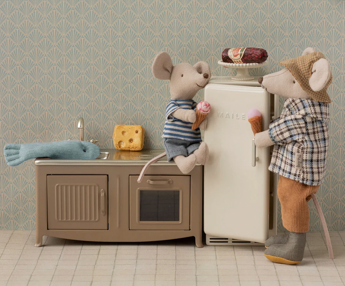 Two toy mice in a kitchen setting with a refrigerator and cabinets.