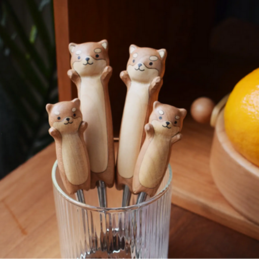 Set of four cat-shaped wooden spoons in a glass container on a wooden surface.