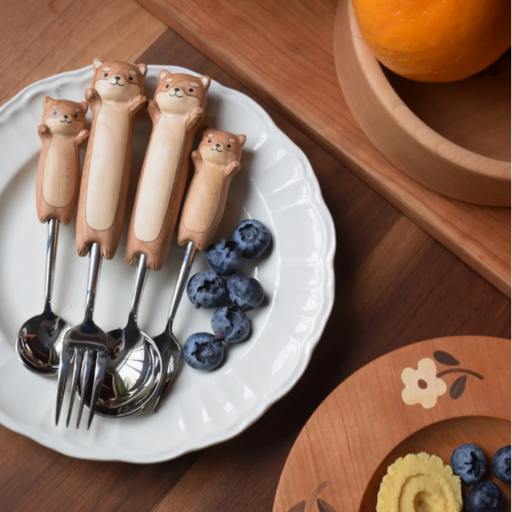 Set of four animal-shaped spoons and forks on a white plate with blueberries, on a wooden table.