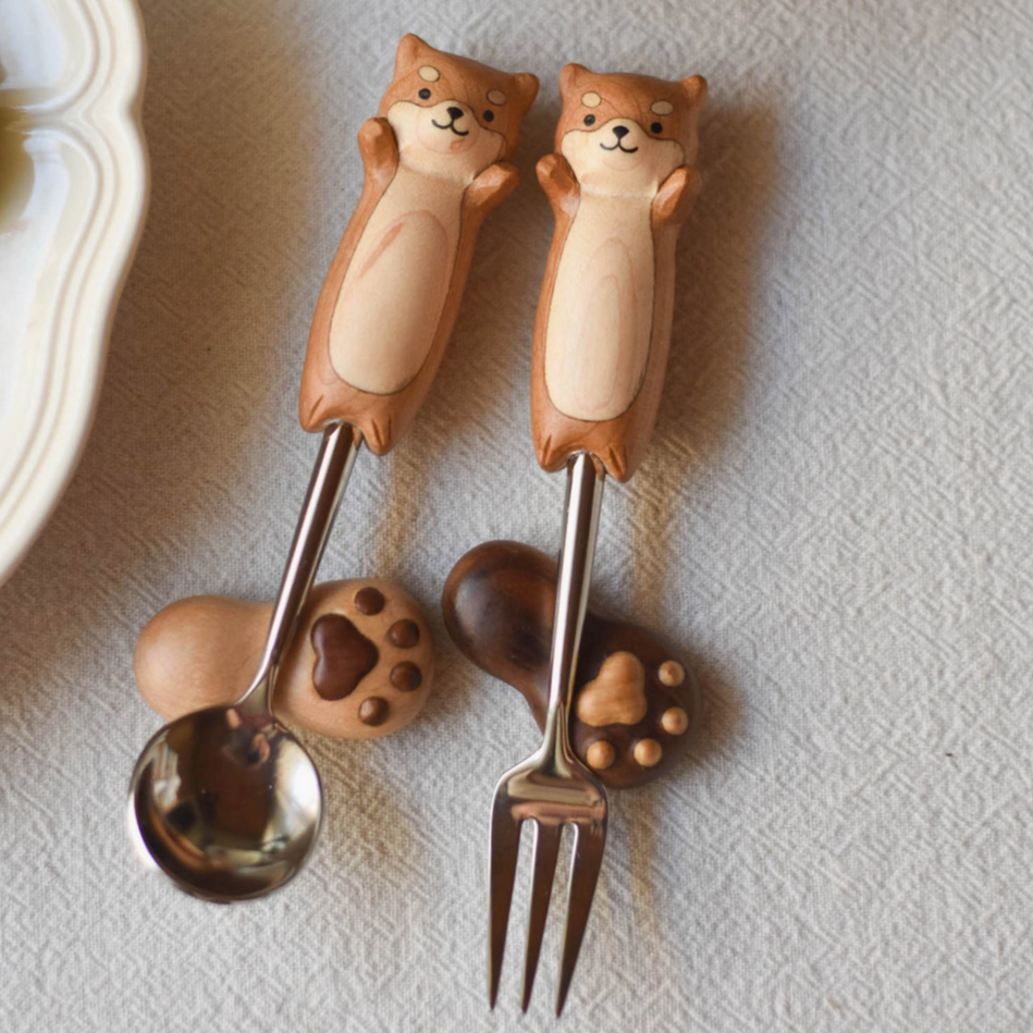 Two dog-shaped spoons with a bowl of fruit and yogurt in the background.